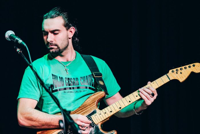 Simeon Boyadjiev, playing guitar, wearing a green tshirt, against a black stage background