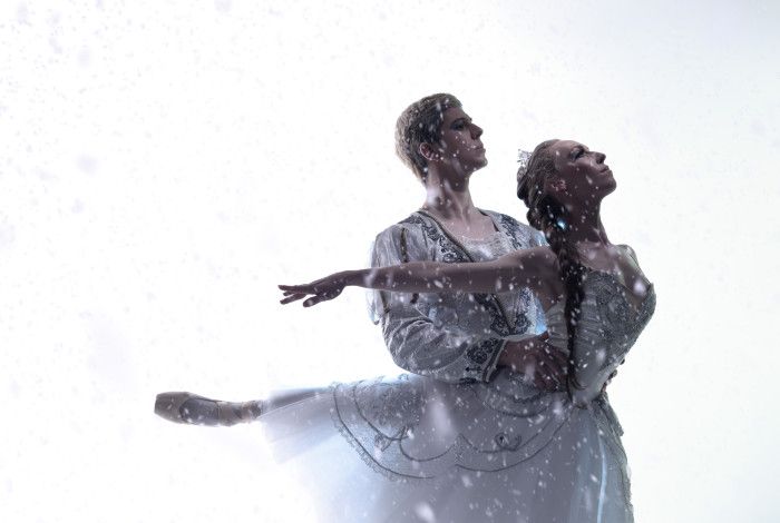 A male and a female ballet dancer, dancing together in white costumes with snow falling around them