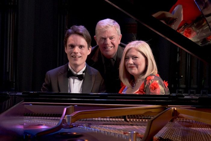 Three performers sitting behind a piano.