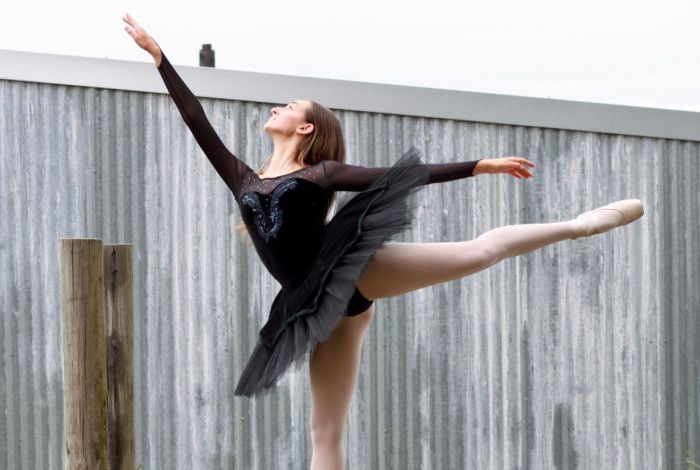 Ballet dancer, posing in elegant and dramatic pointe, outside against a grey wall, in daylight