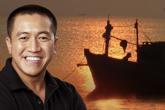 A man smiling Anh Do with a boat in the background