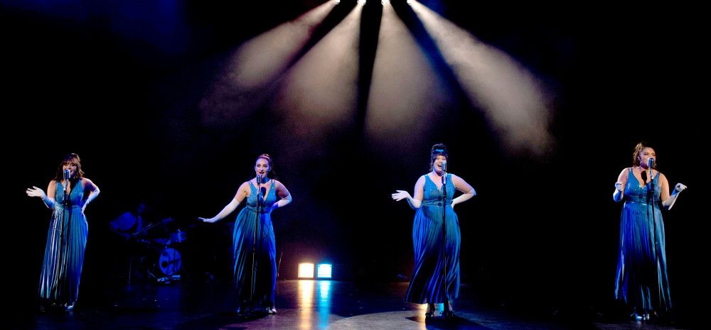 Four women in blue gowns singing onstage