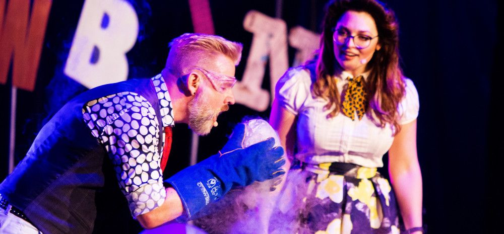 A man holding a round object with dry ice vapour coming off it, while a woman stands nearby watching enthusiastically