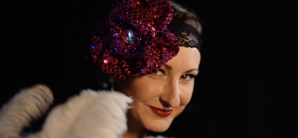 Woman's face in 20s-style sequined headpiece, peeking over the top of large white feathers