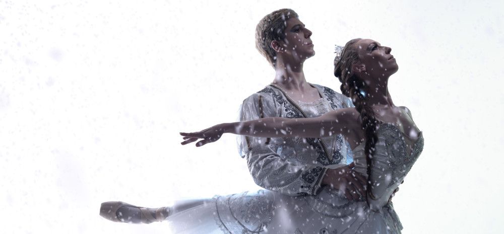 A male and a female ballet dancer, dancing together in white costumes with snow falling around them