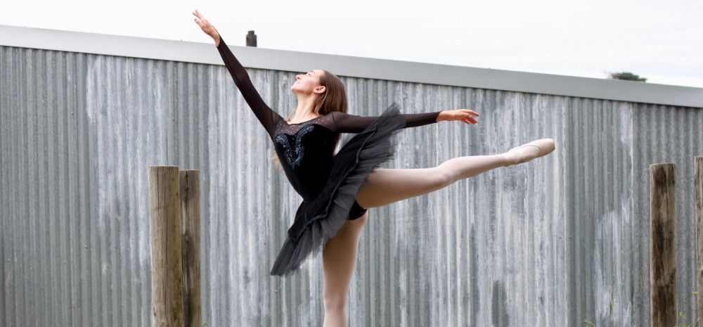 Ballet dancer, posing in elegant and dramatic pointe, outside against a grey wall, in daylight