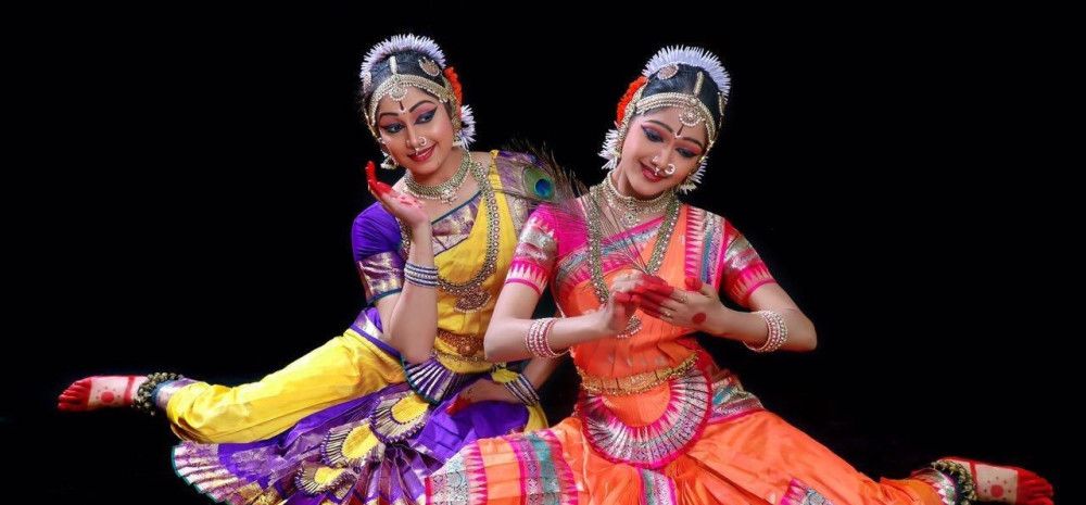 Two women in colourful, traditional dress, striking elegant poses