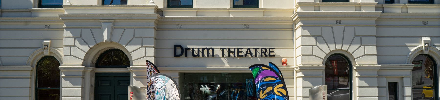 View of the facade of The Drum theatre with plants and flags.